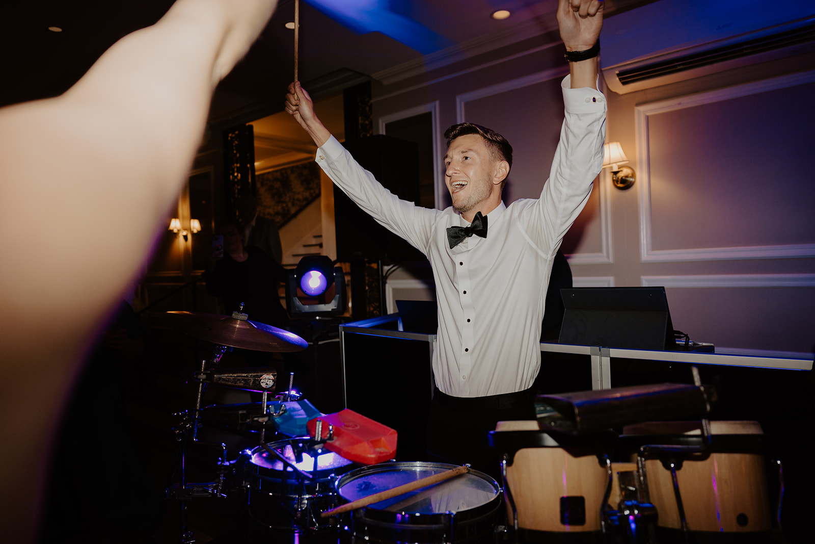 Groom raises drumsticks in celebration while playing live drums on the high-energy reception dance floor.